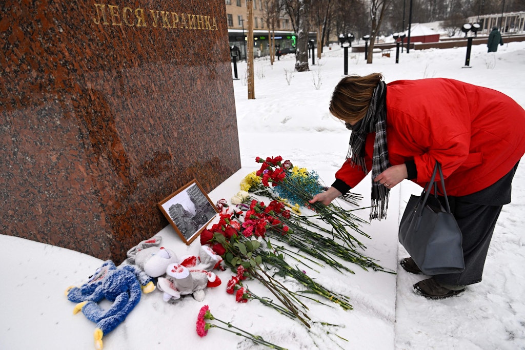 Es begann in Moskau: Eine Frau legt Blumen vor dem Denkmal der ukrainischen Dichterin Lessja Ukrajinka nieder. Angelehnt ist ein Foto des zerstörten Hauses in Dnipro.