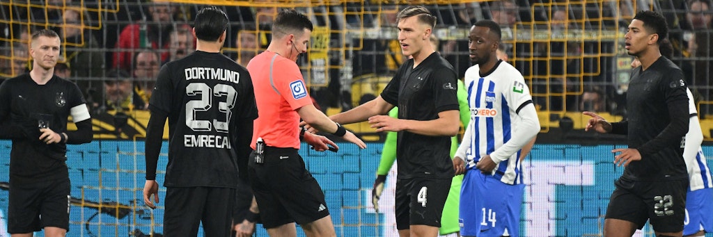Schiedsrichter Harm Osmers versucht den BVB-Spielern und den Profis von Hertha BSC zu erklären, warum er das Spiel minutenlang unterbrach.