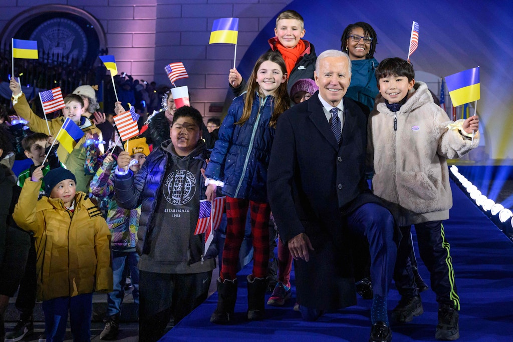 Joe Biden geht in die Knie, um die Kinder nicht zu überragen, die nach seiner Rede mit ukrainischen, US- und polnischen Fähnchen winken.