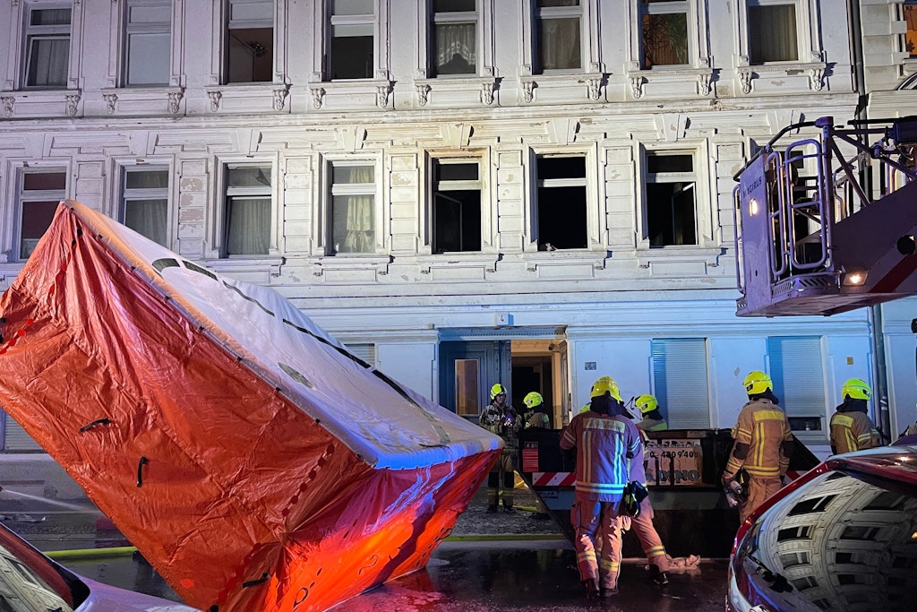 Feuerwehrleute stellen ein Sprungpolster vor dem Haus, in dem es brennt, auf. 