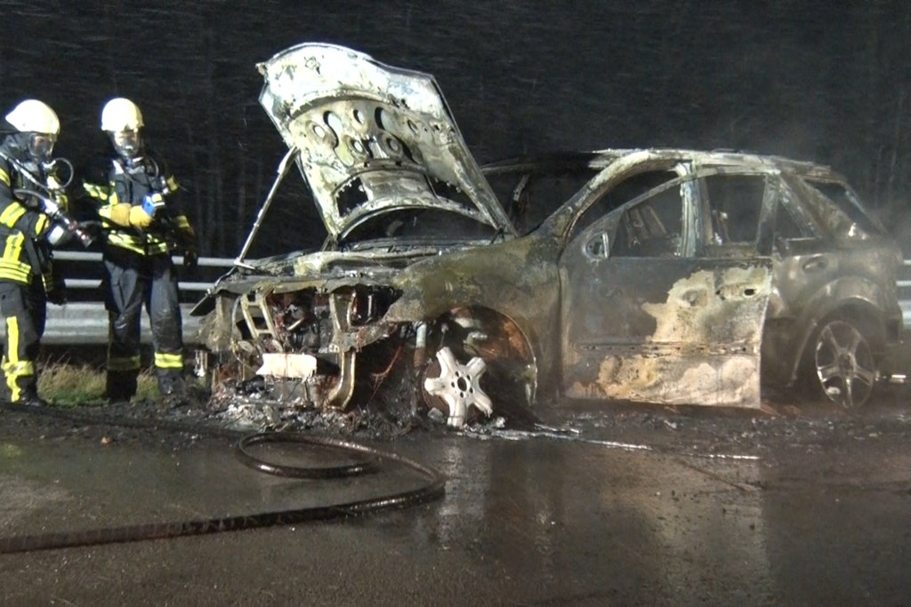 Feuerwehrleute stehen um das völlig ausgebrannte Auto herum.