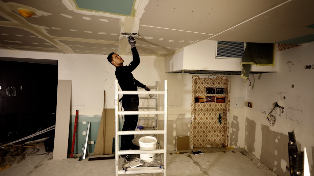 Ein Handwerker streicht die Decke in einem Teil einer originalgetreu nachgebauten DDR-Wohnung auf der Baustelle. Teile der Decke waren durch das Wasser heruntergekommen. 