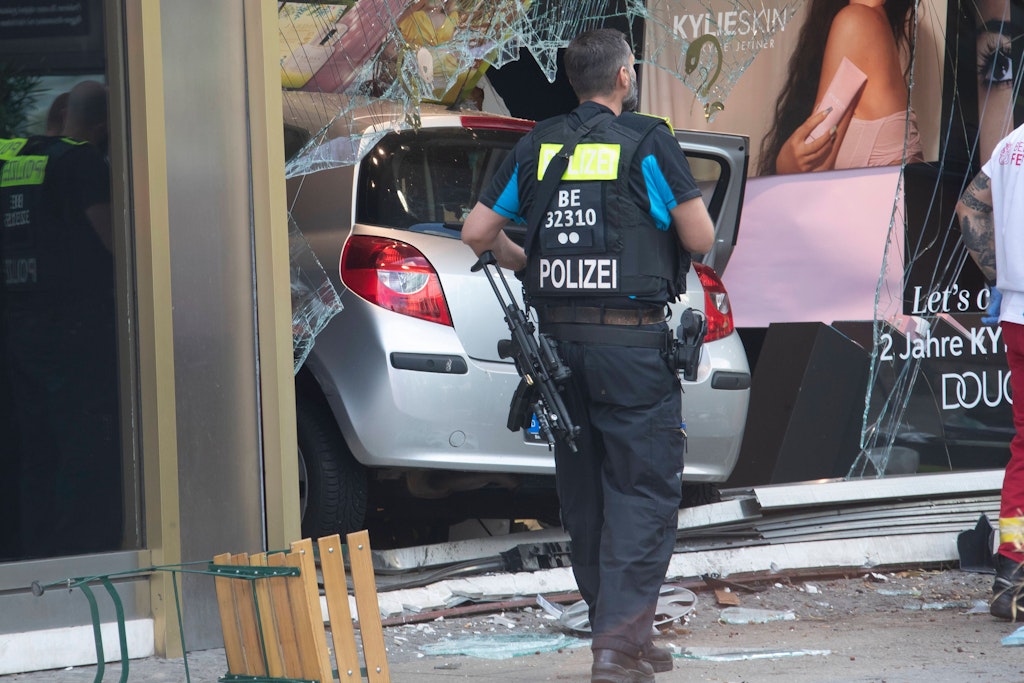 Ein schwer bewaffneter Polizist vor dem Auto des Amokfahrers, das im Schaufenster der Douglas-Filiale am Tauentzien in Berlin steckt. Im Prozess gegen den Amokfahrer sagten am Mittwoch Schüler als Zeugen aus.