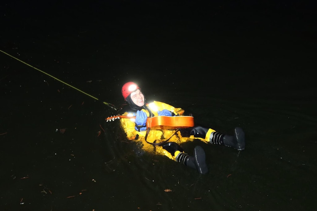 Ein Feuerwehrmann rettet eine Gitarre aus dem Landwehrkanal und probiert sie noch im Wasser aus.
