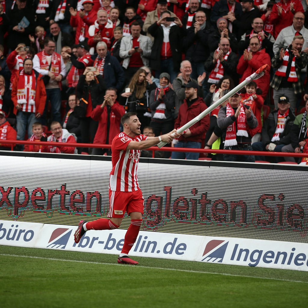Josip Juranovic feiert den Sieg des 1. FC Union auf seine Weise, indem er eine Eckfahne zu einem Winkinstrument umfunktioniert.