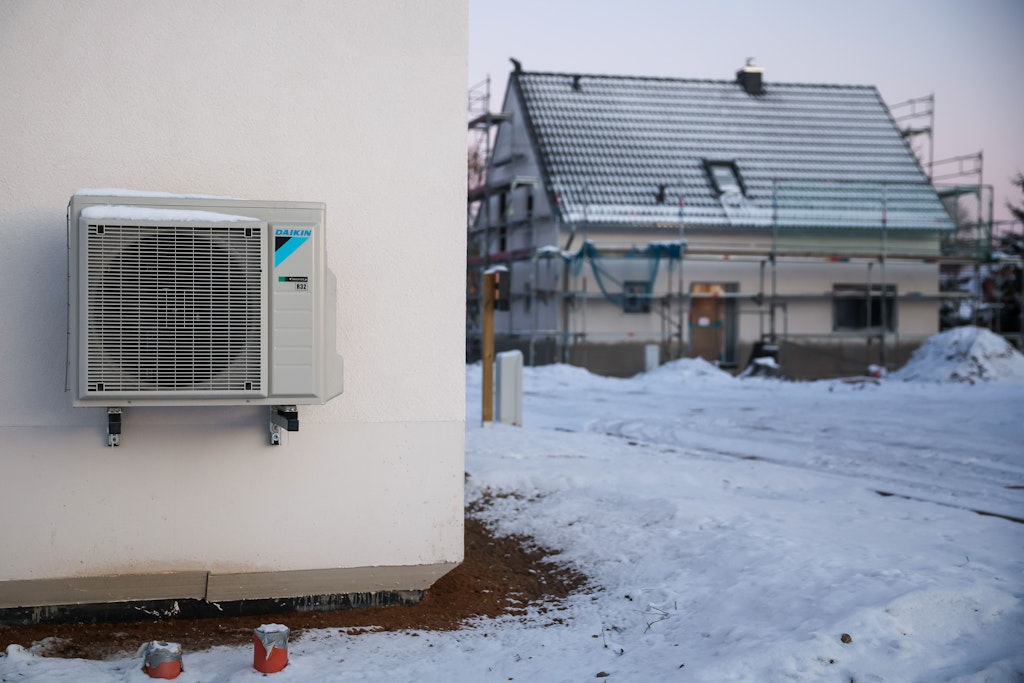 Eine Luftwärmepumpe hängt bei Schnee und Eis an einer Hauswand in einem neu entstehenden Einfamilienhausgebiet. (Archivfoto). 