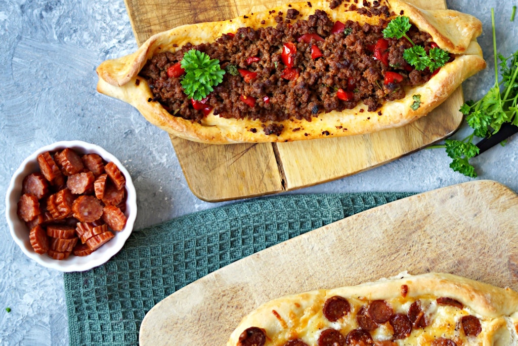 Die Fladenbrot-Schiffchen werden mit einer Paprika-Hackfleisch-Mischung oder mit Käse und Kabanossi-Wurst gefüllt.