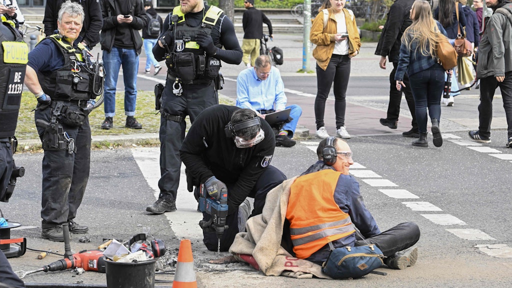 Und der Aktivist grinst: Am Ernst-Reuter-Platz musste am Montag sogar der Asphalt zerstört werden, um dem Klima-Kleber von der Straße zu lösen. 