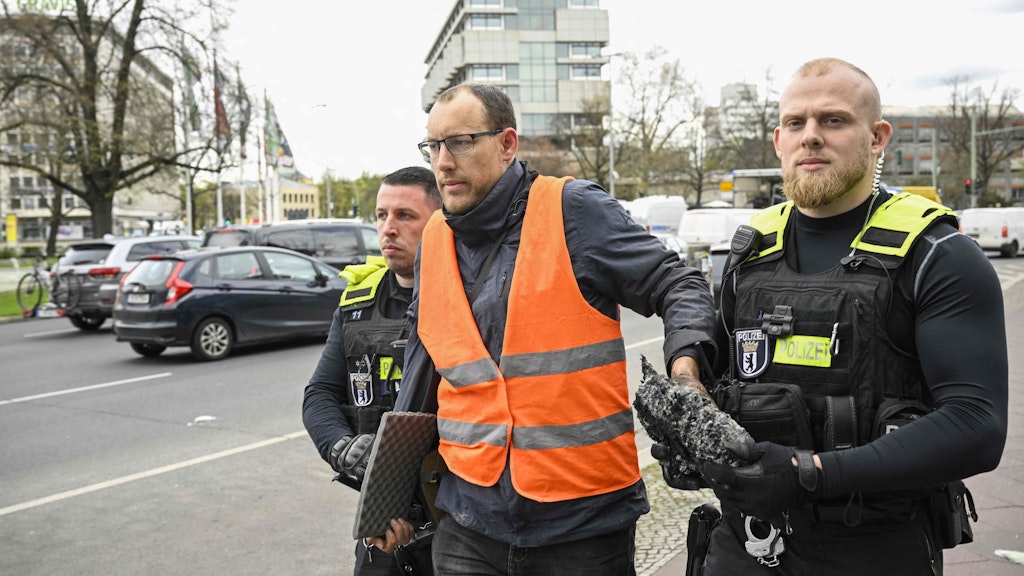 Am Ernst-Reuter-Platz wird ein Aktivist abgeführt. Er musste von der Polizei mittels einer Säge von der Fahrbahn gelöst werden. An seiner Hand klebt noch ein Stück Asphalt.