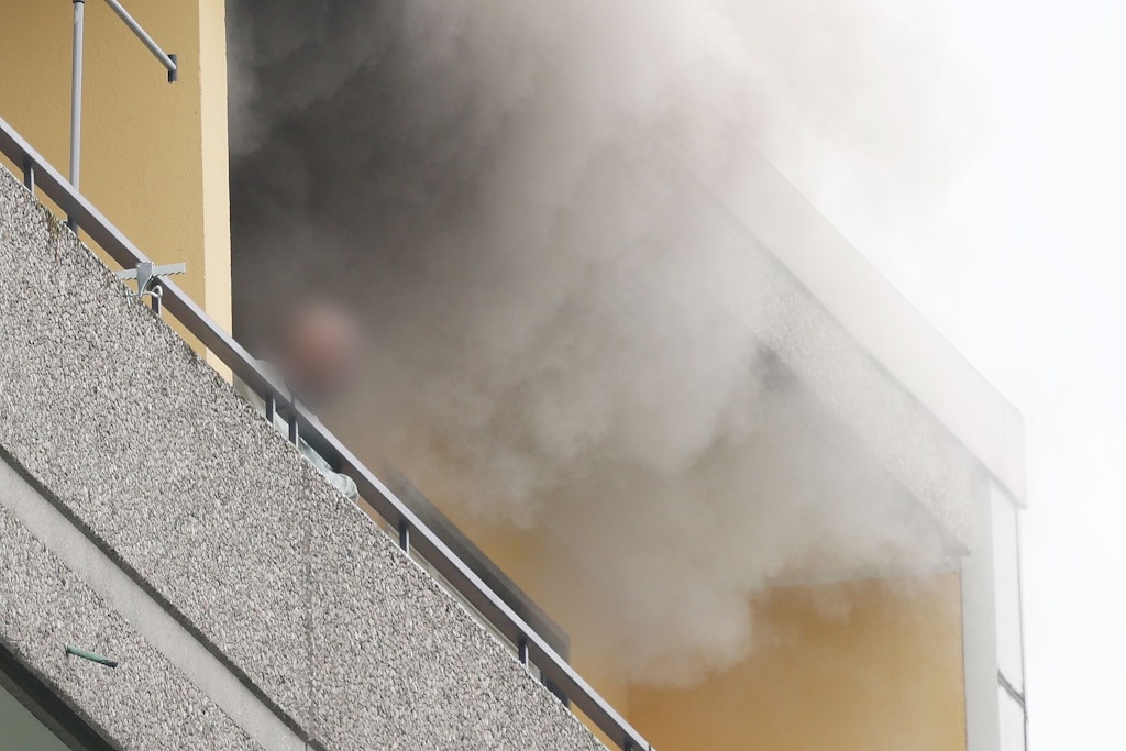Eine Person steht auf dem Balkon von einem Hochhaus, aus dem Rauch quillt. Bei einer Explosion in einem Hochhaus in Ratingen am Donnerstagvormittag wurden mehrere Menschen verletzt.
