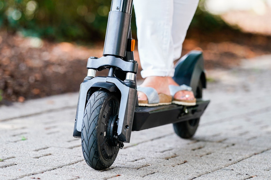 Eine Person in Sandalen auf einem E-Scooter.