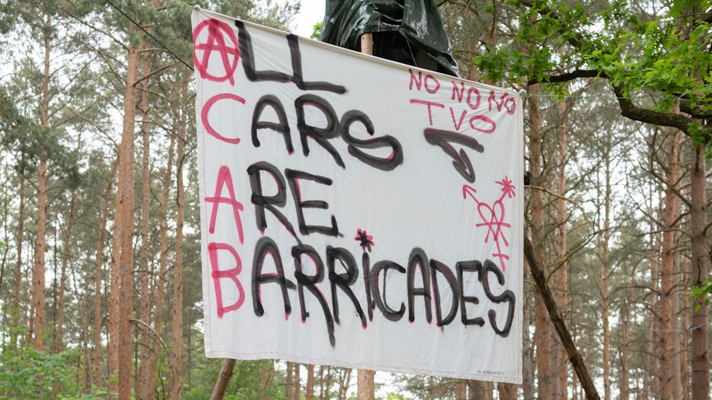 Ein Transparent mit der Aufschrift „All Cars are Barricades“ (Alle Autos sind Barrikaden) hängt an einem Baumhaus in einem Waldstück in der Wuhlheide.