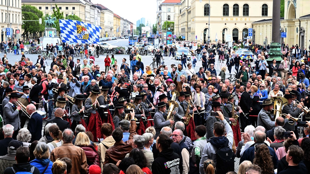 Musiker in traditionellen Trachten verlassen nach der Hochzeit die Theatinerkirche und gehen durch das Publikum über den Odeonsplatz.