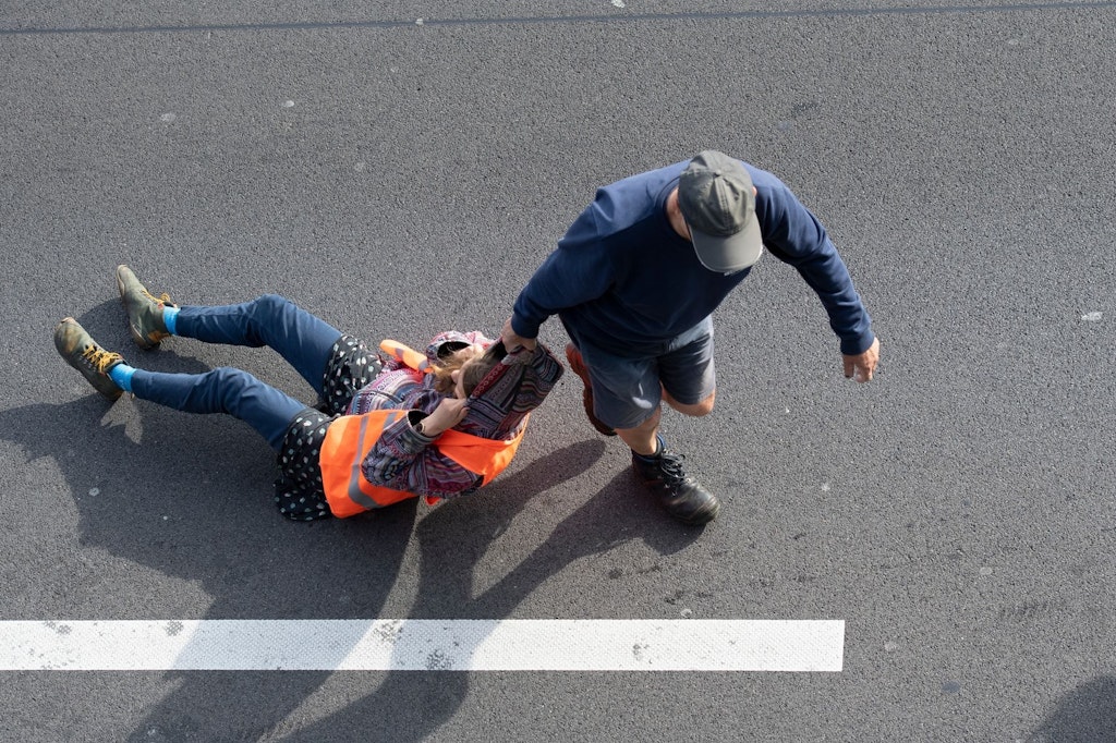 Ein dpa-Fotograf war zur Stelle, als ein aufgebrachter Verkehrsteilnehmer am Freitag bei einer Blockade der Letzten Generation auf der Autobahn 100 eine Aktivistin von der Straße zerrte.