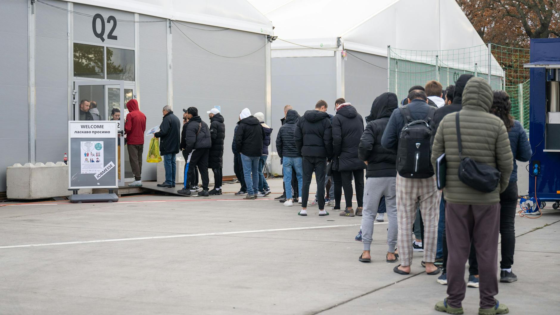 Am ehemaligen Flughafen Tegel stehen Geflüchtete Menschen vor einer Leichtbauhalle.