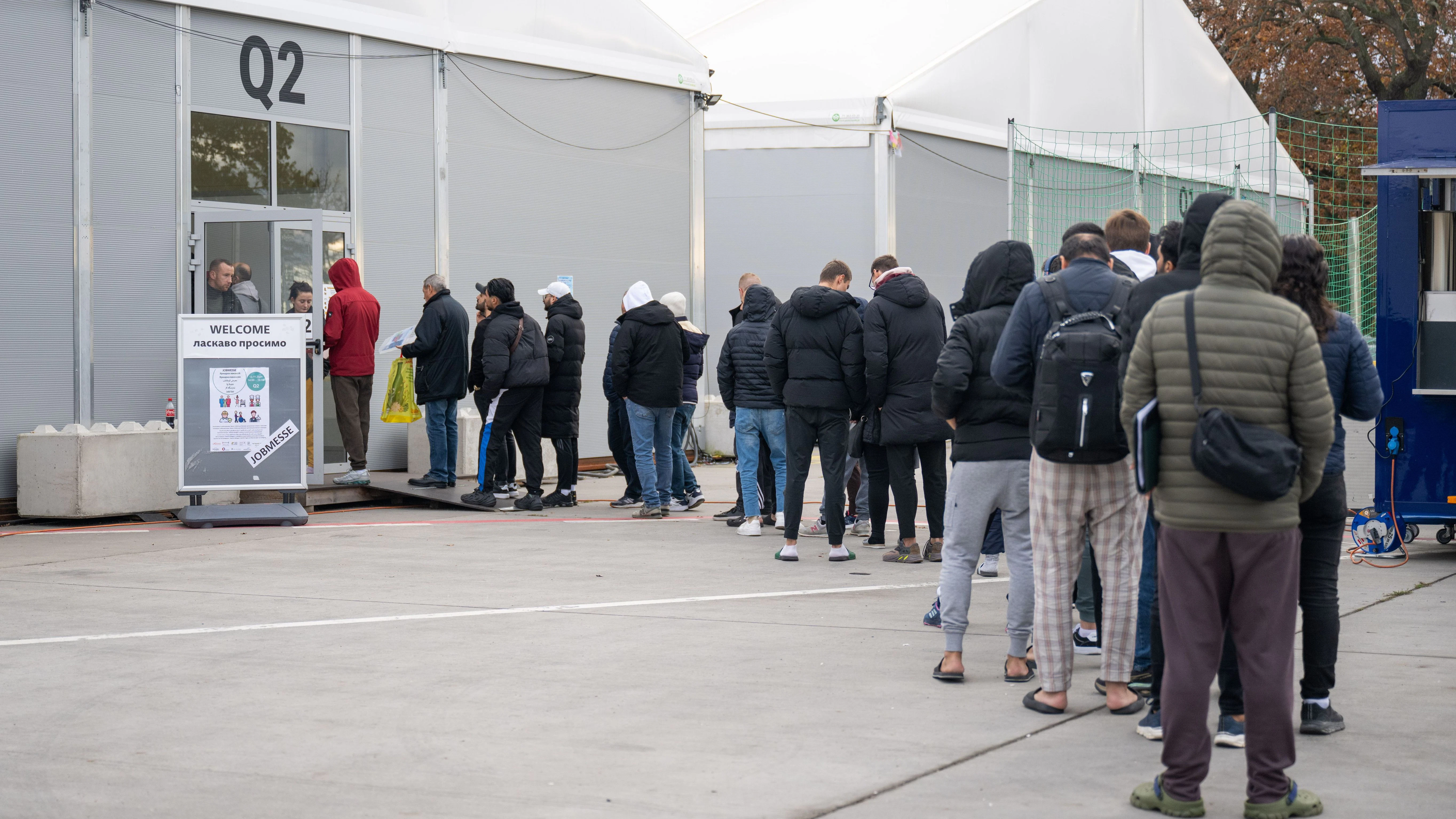Am ehemaligen Flughafen Tegel stehen Geflüchtete Menschen vor einer Leichtbauhalle.