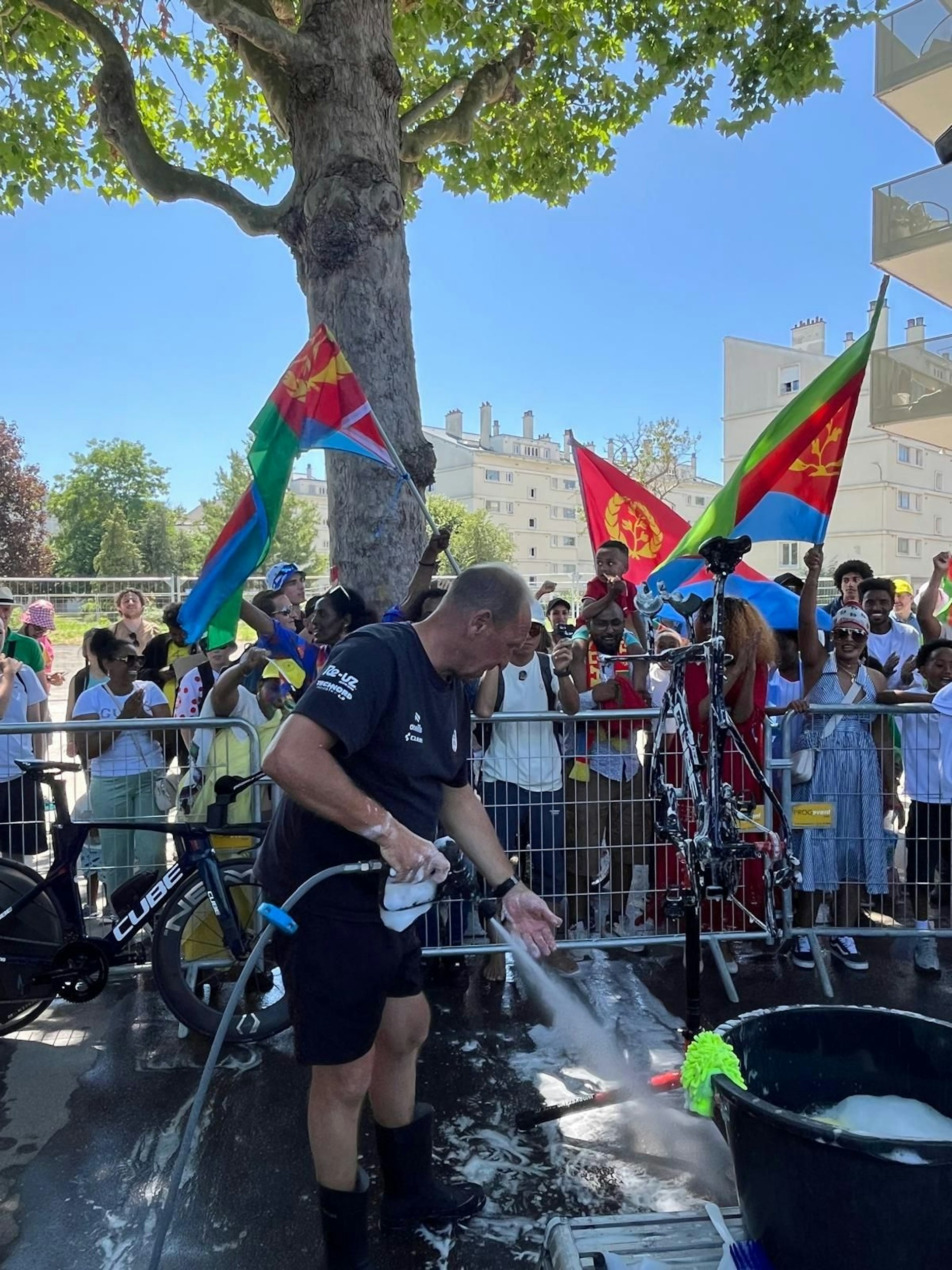 Hinterm Zaun schwenken eritreische Fans die Nationalfahnen für Landsmann Biniam Girmay.