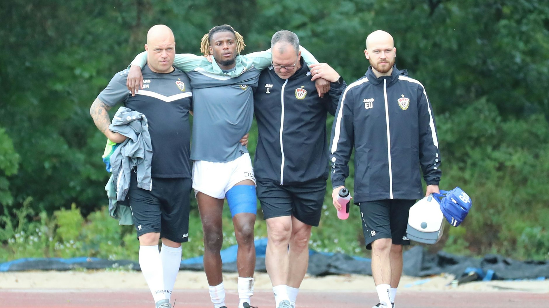 Zeugwart Stefan Malchow (l.) und Teammanager Jörn Lenz stützen Américo Neves. rechts Physiotherapeut Elias Ulsamer.