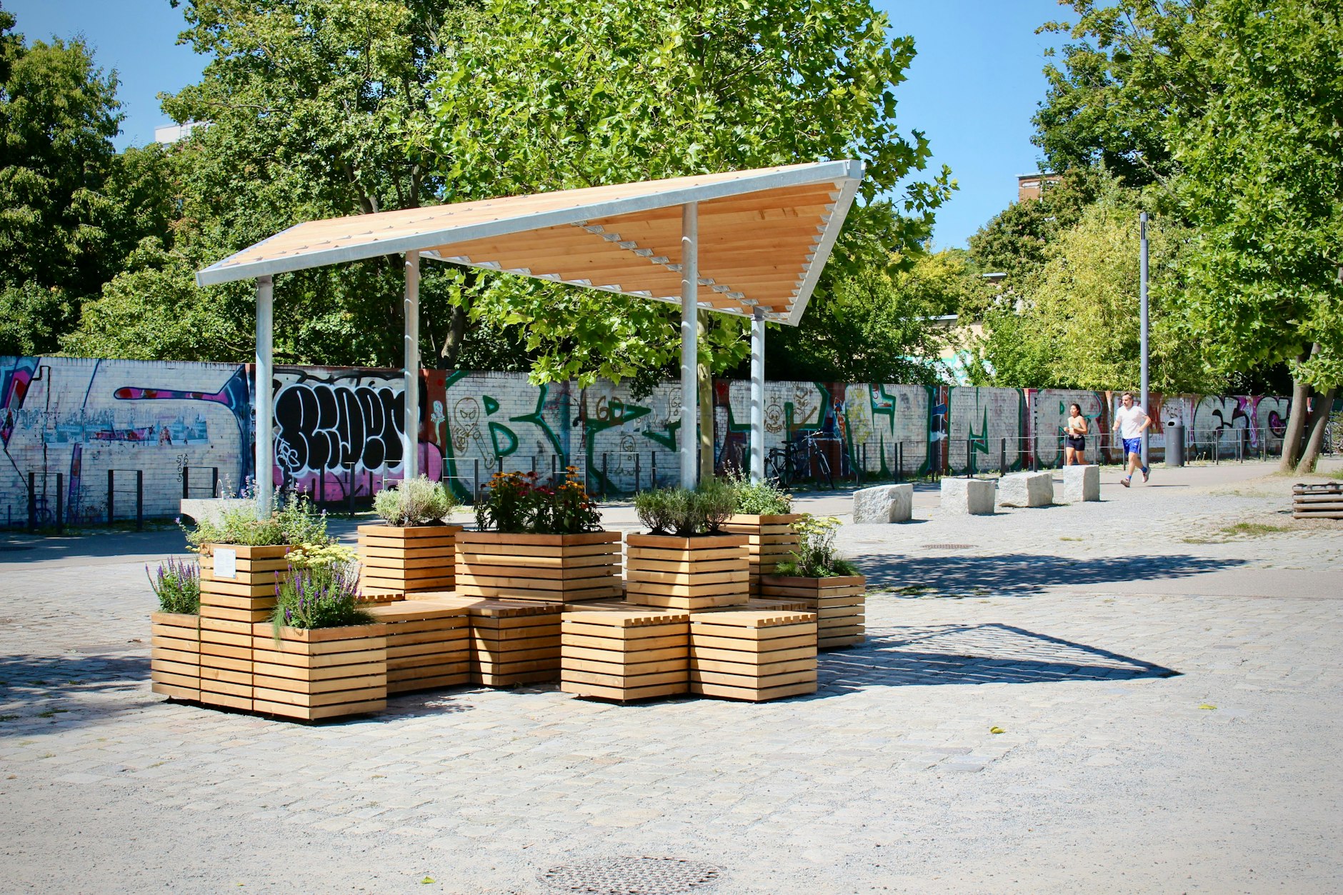 Am Berliner Cooling-Point fällt das Licht durch das halb durchlässige Dach. Bei dem zum Abkühlen konzipierten Ort bleibt der Schatten laut Besuchern oft zu schwach. Zudem liegen etwa die Hälfte der Sitzplätze in der prallen August-Mittagssonne. Es sind um die 30 Grad. Die Besucher weichen in den Schatten der nahen Bäume aus.